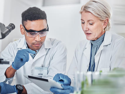 Two people in white lab coats discussing something on a tablet.