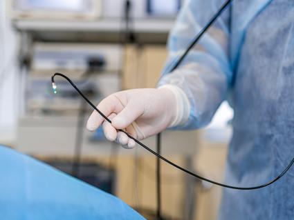 A partial image of a doctor holding a colonoscope near a patient in the endoscopy suite.