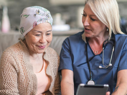 A female patient wearing a headscarf sits next to a female physician. The physician is showing the patient a wireless tablet.