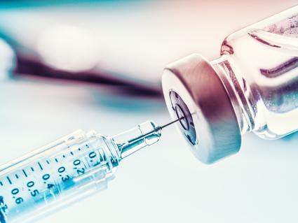 A photograph of a syringe drawing medicine from a glass vial.