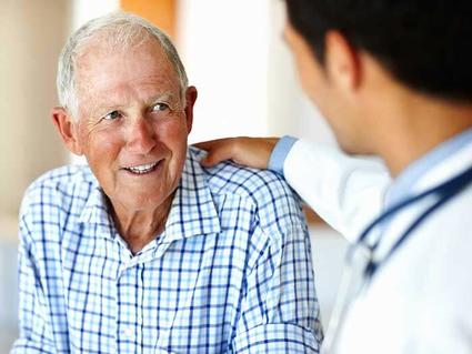 Man with white hair smiles at a male doctor who faces him and has a hand on the man's shoulder.