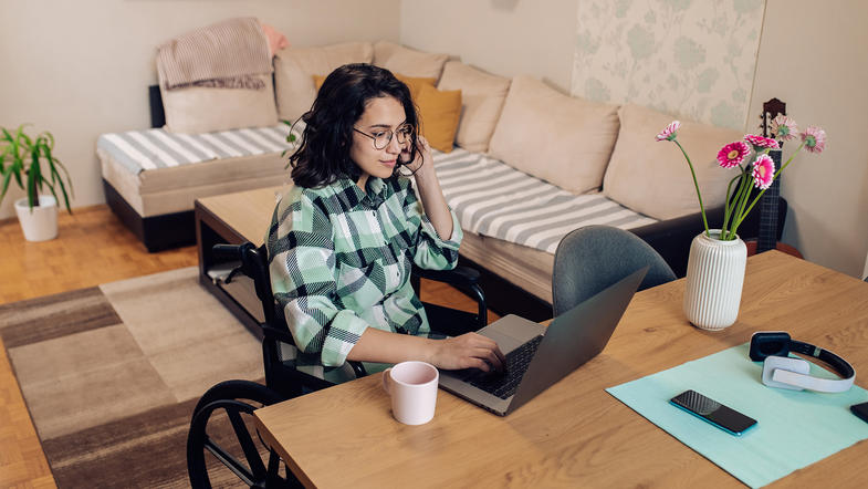 Young woman in a wheelchair talking on phone from her home office