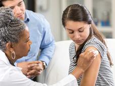 A teenage girl receiving a vaccine in her upper arm from a nurse.