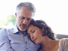 Woman seated beside man, eyes closed and leaning her head on his chest