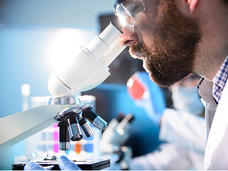 A scientist wearing safety goggles is intently observing through a microscope in a laboratory setting.