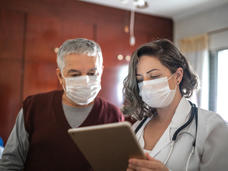 Male patient and female doctor wearing masks view a tablet together.