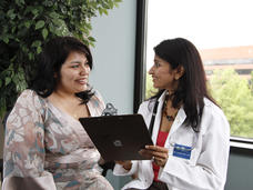 Un médico con una computadora en las manos habla con una mujer.