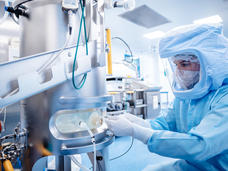 A technician in full body protective gear adjusting a machine for making mRNA vaccines.
