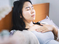 Woman laying in bed, hand on chest, in discomfort.