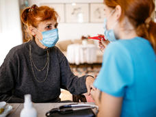 A young female community health worker taking a patient's temperature in her home.