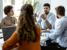 Team meeting with employees sitting at a table with their laptops open