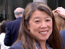 An Asian woman with light skin tone wearing a blue blazer (Dr. Mignon Lee-Cheun Loh) smiles at the camera at an outdoor conference event. 