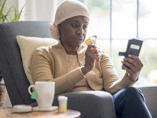 Woman wearing a head scarf holding a bottle of medication in one hand and looking at her phone in the other hand.