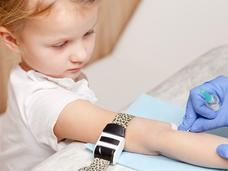 A young girl with her arm out and gloved hands cleaning a spot on her arm with a swab.