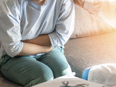 Photo of a woman sitting on a couch, leaning slightly forward, with arms folded over abdomen.