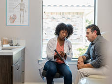 A female doctor points to something on tablet as a male patient listens.