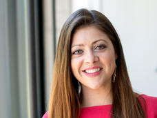 A woman, Dr. Aubrey Hubbard, with long brown hair and hazel eyes wearing a pink blouse and long earrings stands smiling at the camera.