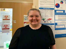 Bonnie Yates standing in a hallway with scientific data and graphs posted on the wall in the background.