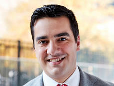 A man, Dr. Michael Ortiz, with brown hair and brown eyes and wearing a grey suit with a red tie, smiles at the camera.