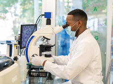 Man in a white lab coat looking into a microscope