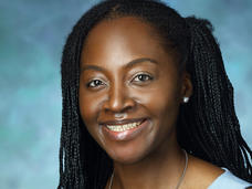 A woman, Dr. Ethel Ngen, with braided black hair and dark brown eyes wearing a light blue blouse smiles at the camera.