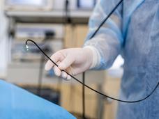 A partial image of a doctor holding a colonoscope near a patient in the endoscopy suite.