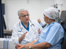 A female patient with an IV in her arm has a conversation with a male doctor. 