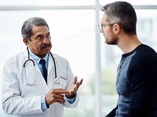 An older male doctor talking with a middle-aged male patient.