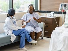 A middle-aged black woman in a hospital gown talking with a surgeon.