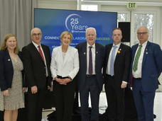 image of people standing in front of a banner advertising the 25th anniversary of the Ireland, Northern Ireland, National Cancer Institute Cancer Consortium. 