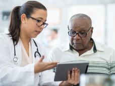 A young female doctor shows information on a tablet computer to an older black male patient.