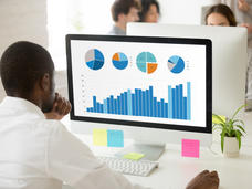 A man looks at data charts and graphs on a computer screen in an office.