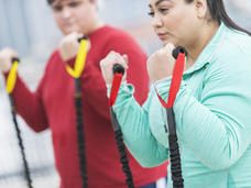 A Hispanic woman in light blue clothes doing curls with exercise bands.