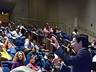 A presenter speaks in front of a large audience