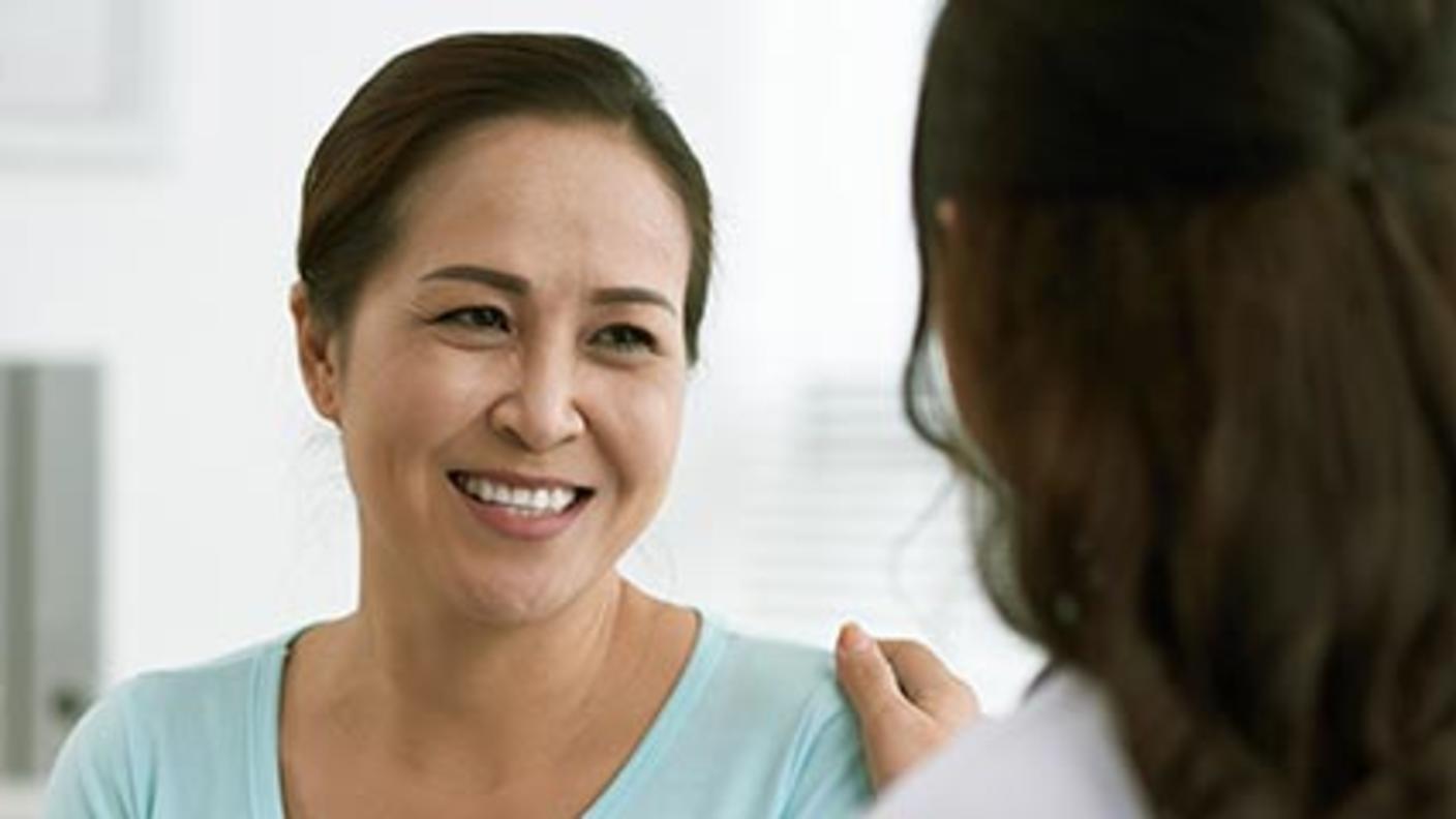 Woman smiles at her health care provider, whose hand rests on her shoulder.