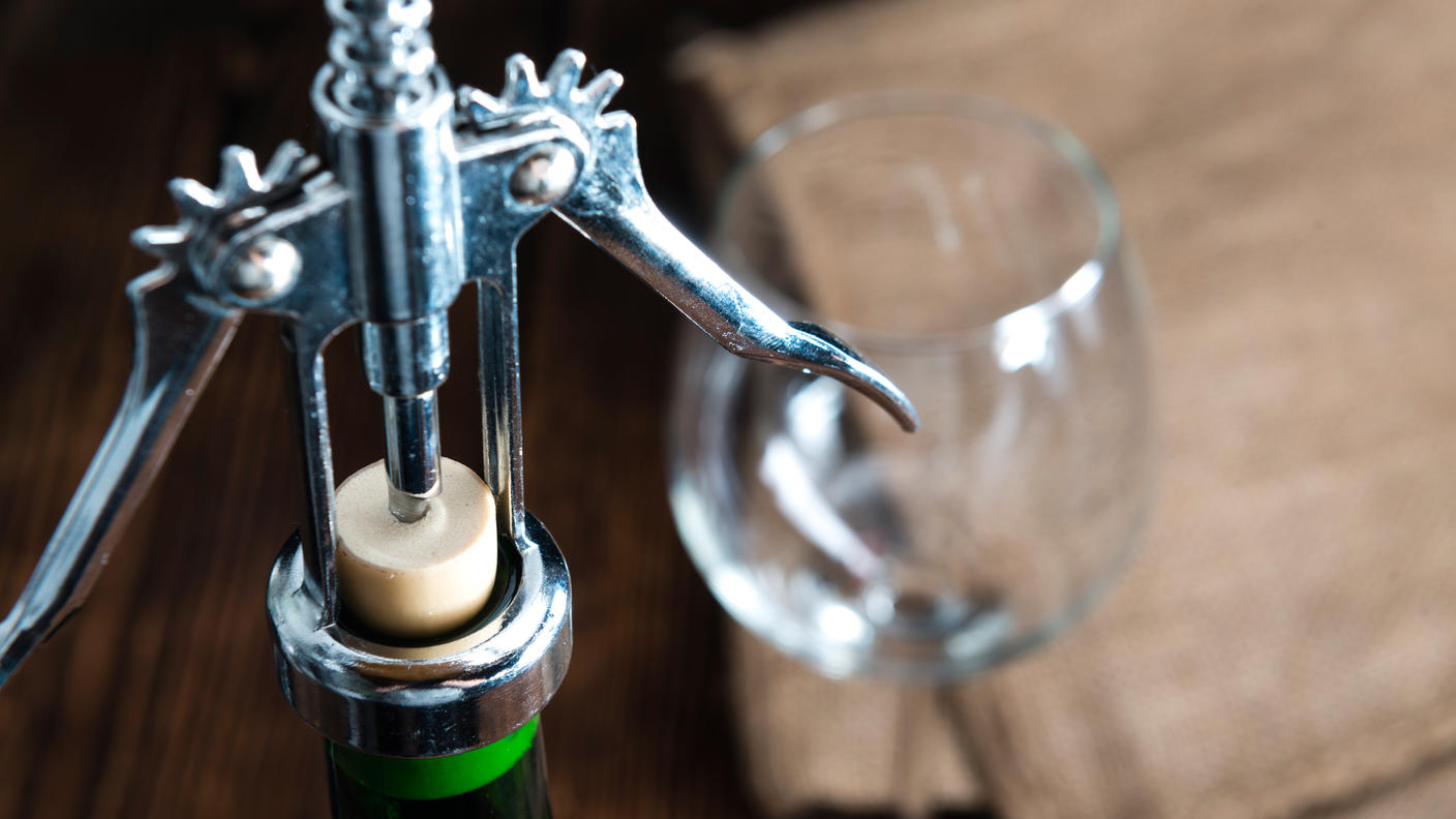 A bottle of wine being opened with a metal opener.