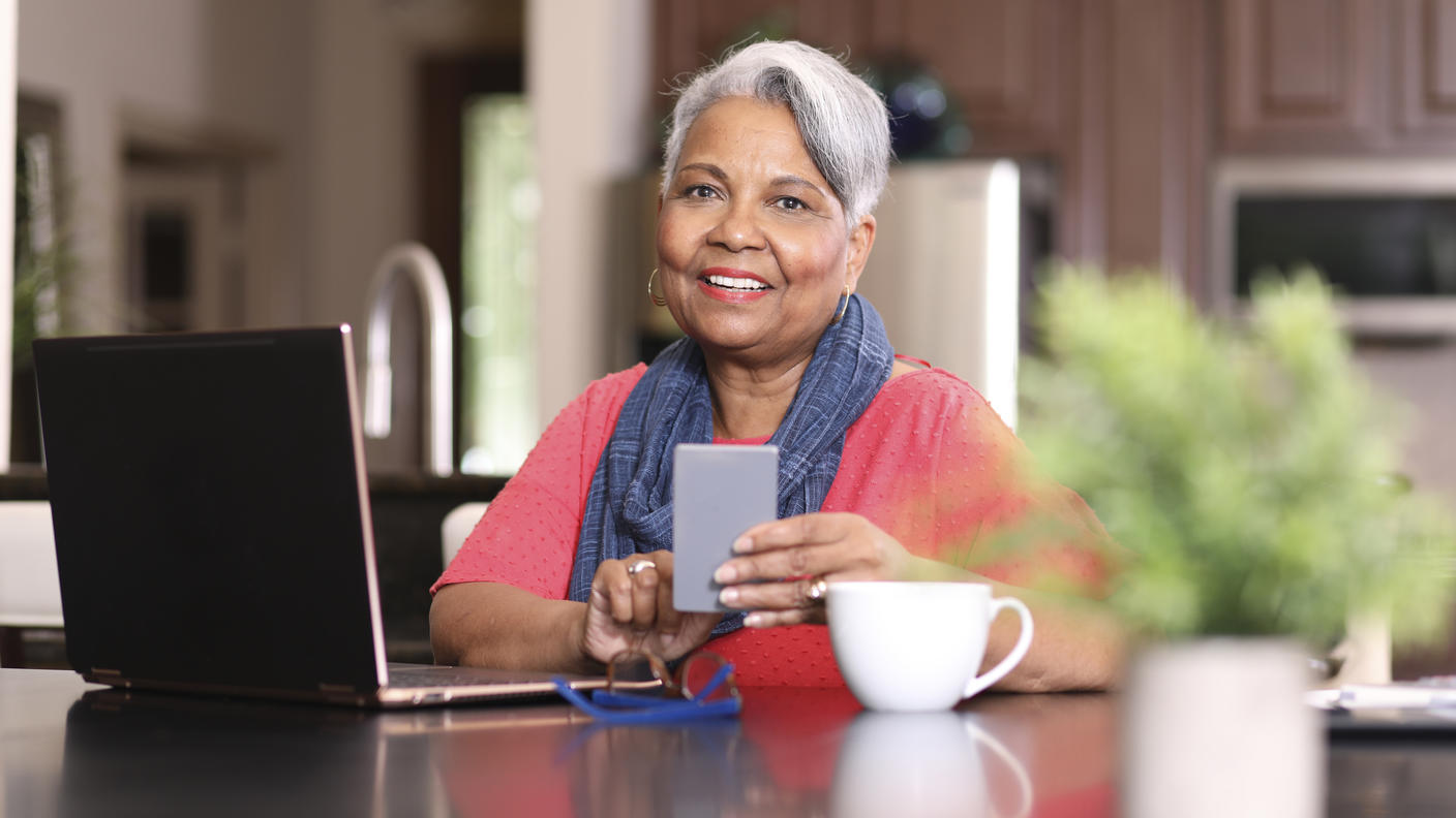 Woman sitting in front of a laptop and holding a smart phone.