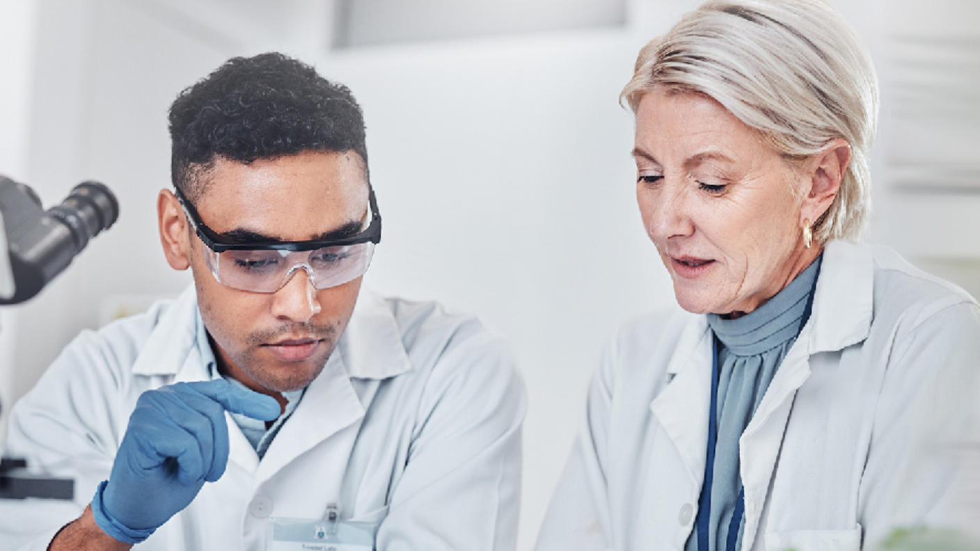 Two people in white lab coats discussing something on a tablet.
