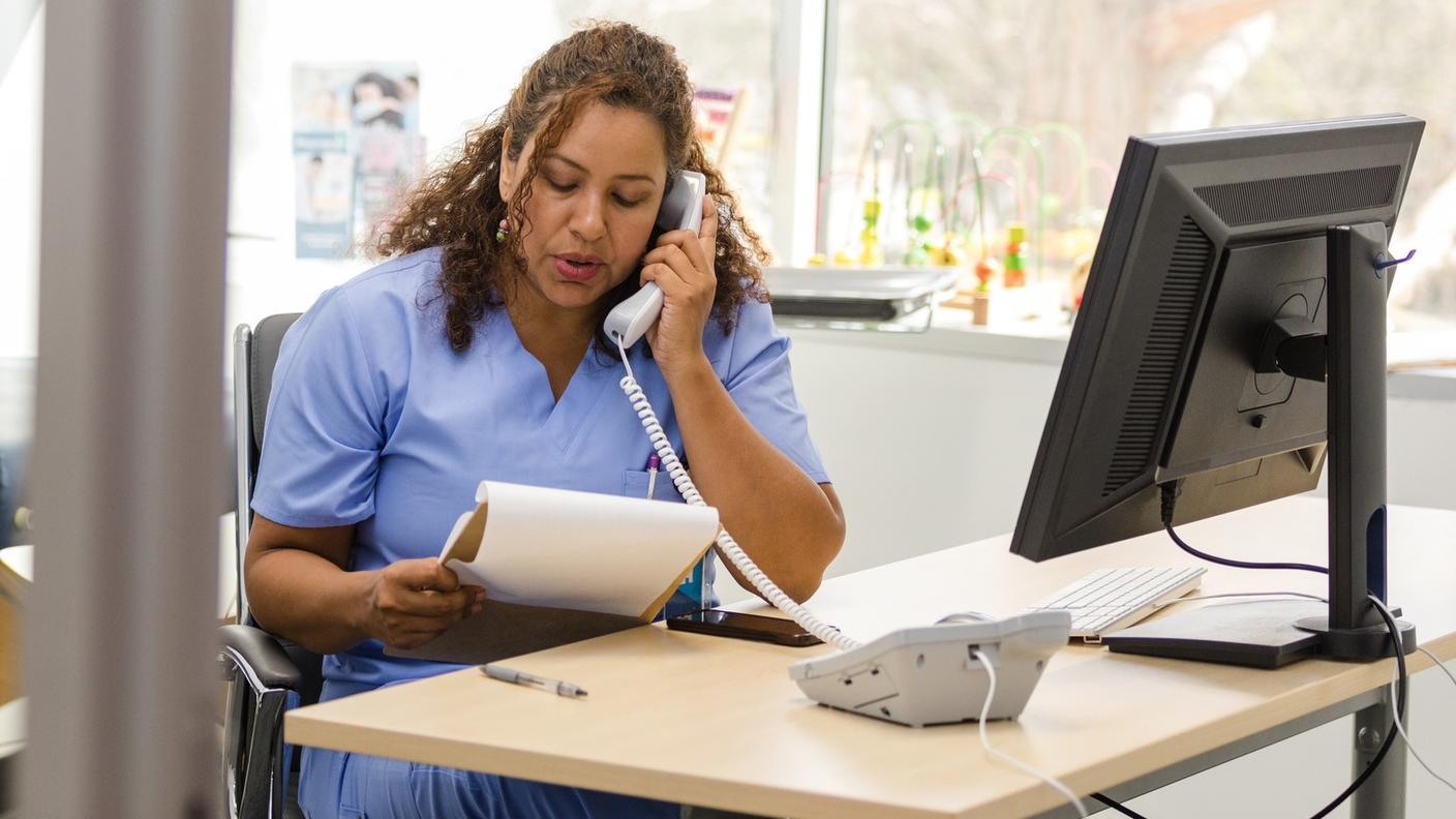 Una mujer con uniforme azul en un consultorio habla por teléfono.
