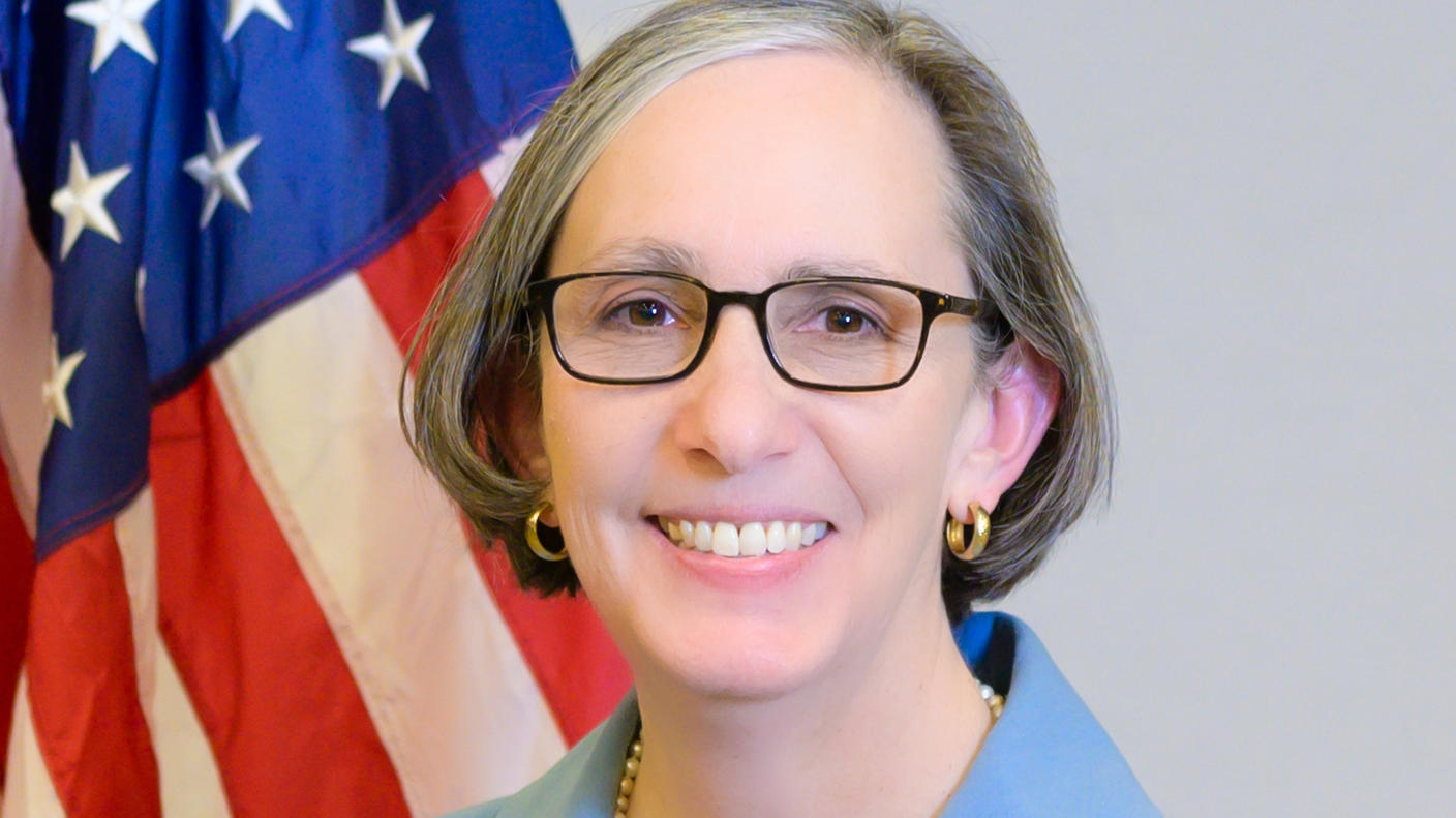 NCI Director Dr. Rathmell stands in front of the U.S. flag