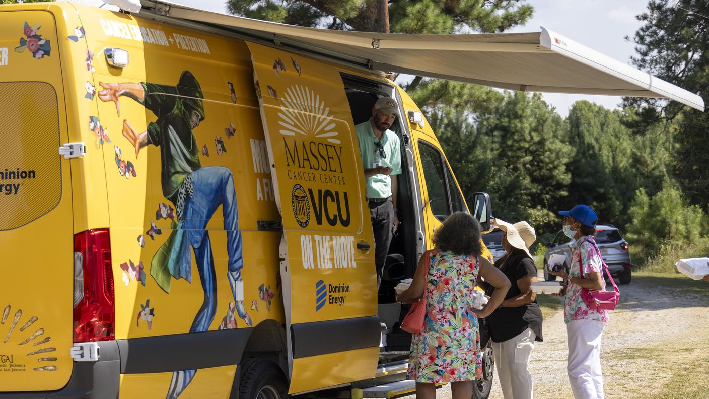 Se observa una camioneta decorada en colores brillantes donde un trabajador de salud conversa con varias personas.