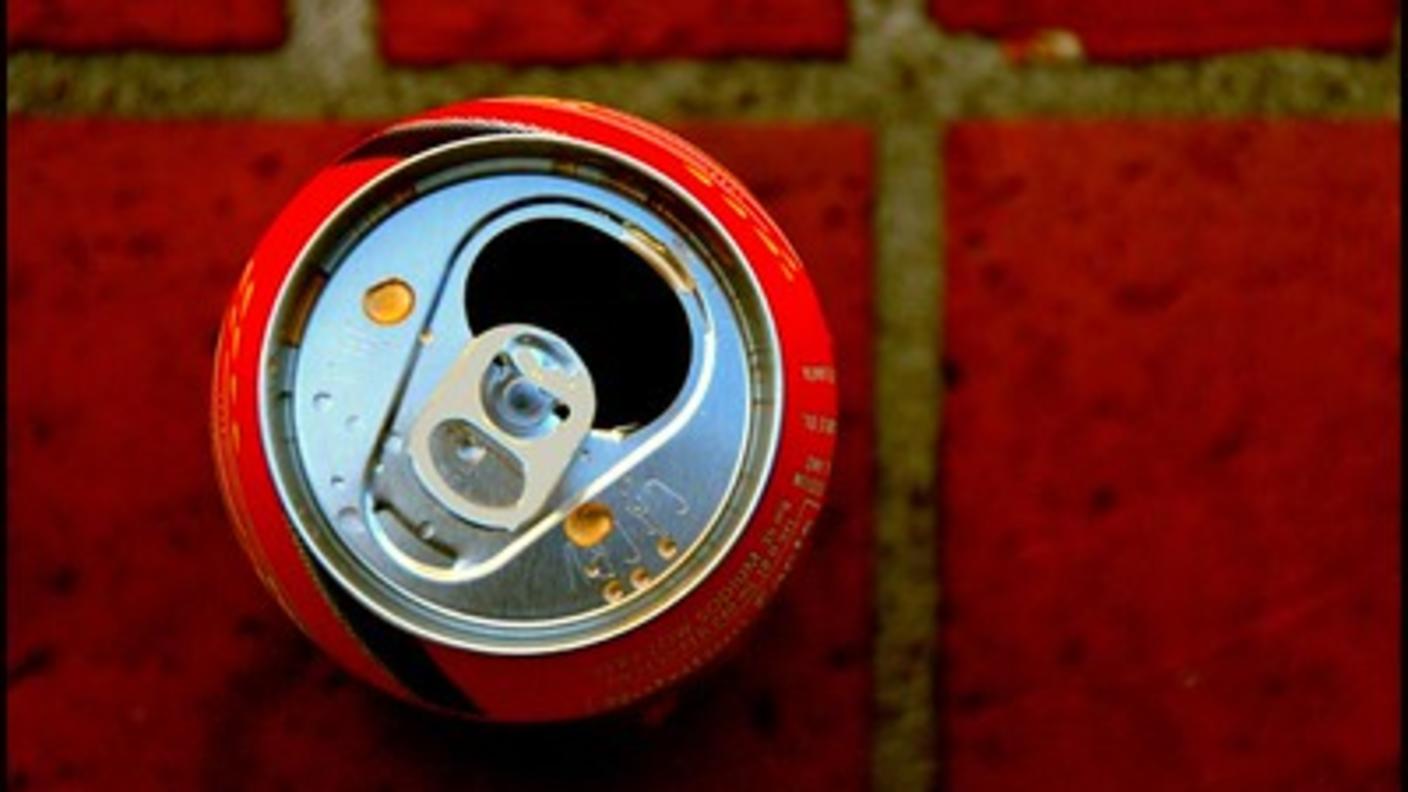 A photo of a red soda can, taken from directly above, sitting on a dark red tiled floor.