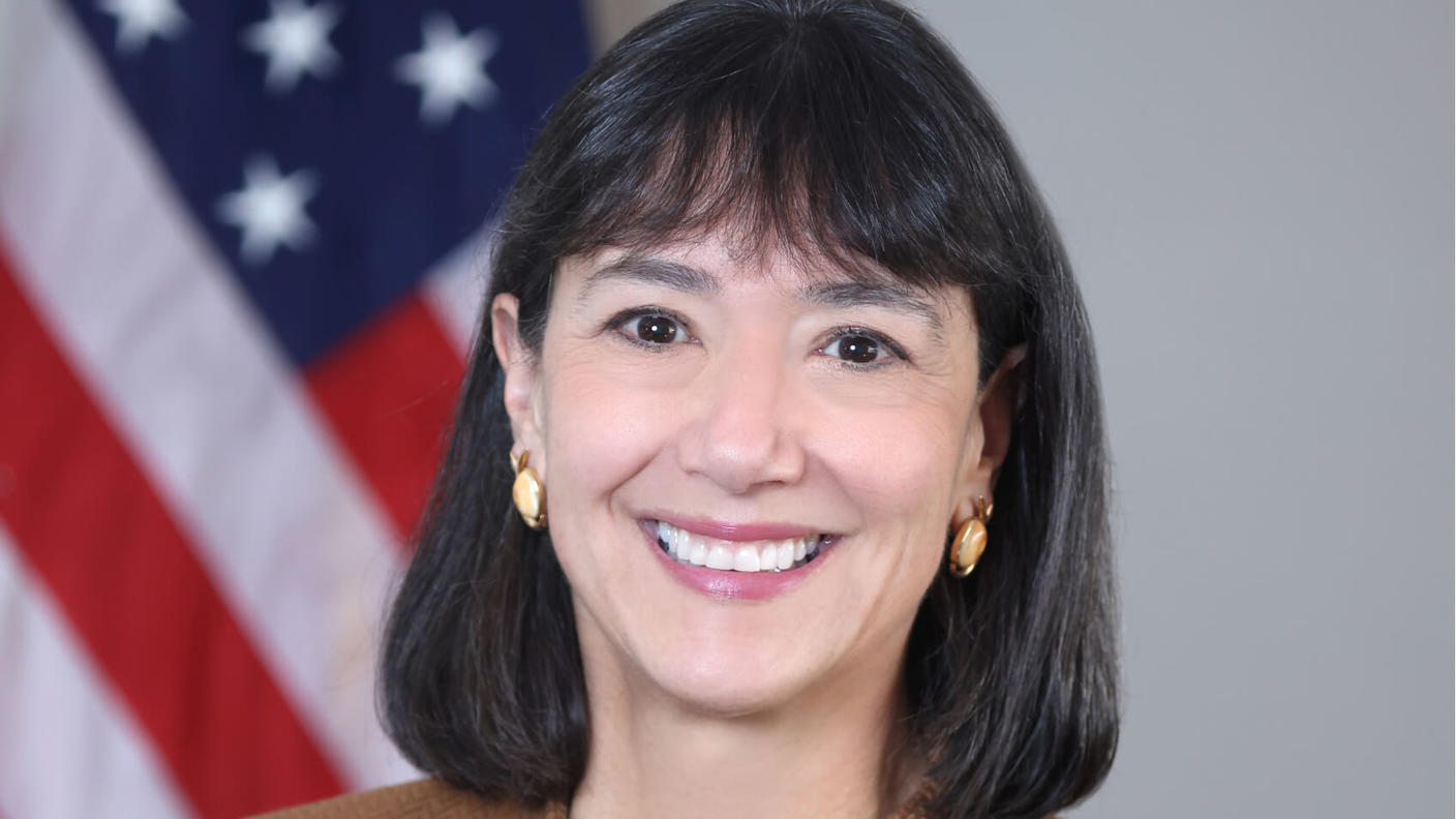 Woman (NCI Director Dr. Monica Bertagnolli) with dark hair wears a brown jacket over a patterned top and smiles at the camera.
