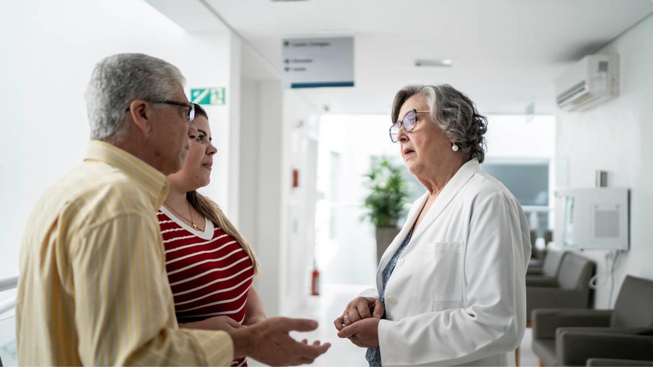 Un paciente de cáncer y su cuidadora hablan con una médica.
