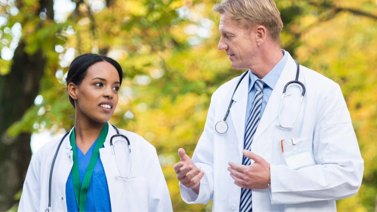 Una médica y un médico conversan mientras caminan al aire libre.