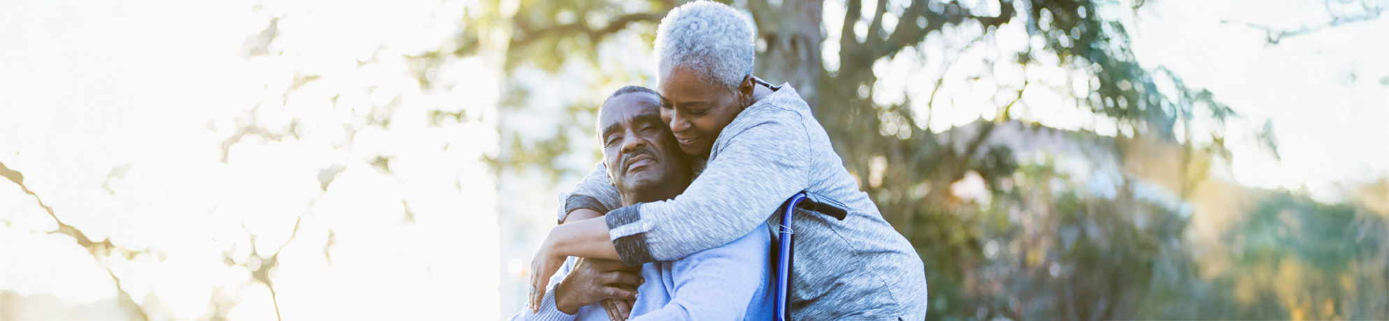 Una mujer abraza a su marido sentado en silla de ruedas.