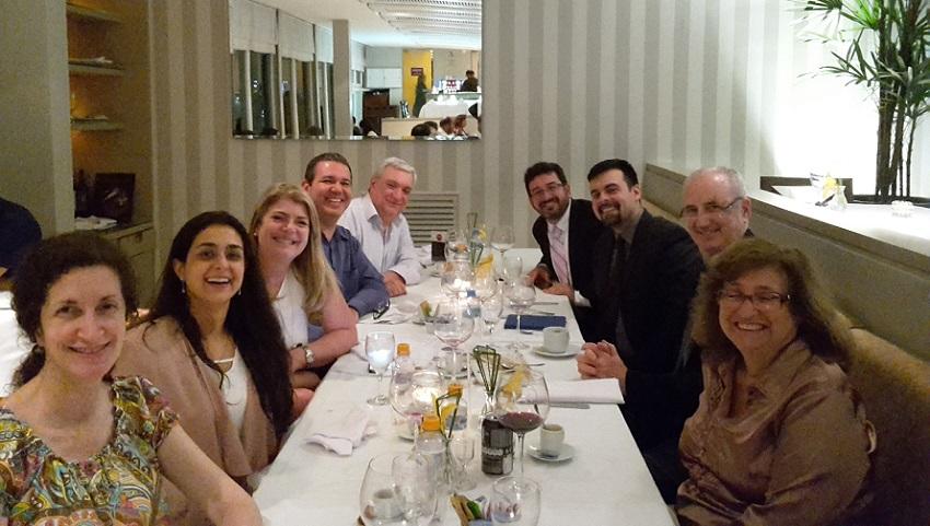 Dr. Claudia Bessa, Dr. Ana Cristina Pinho Mendes Pereira, Marcelo Soares, João Viola, João Viegas, Doug Perin, Dr. Ted Trimble, and Dr. Eliana Abdelhay sit together, smiling for the camera around a dinner table at a restaurant