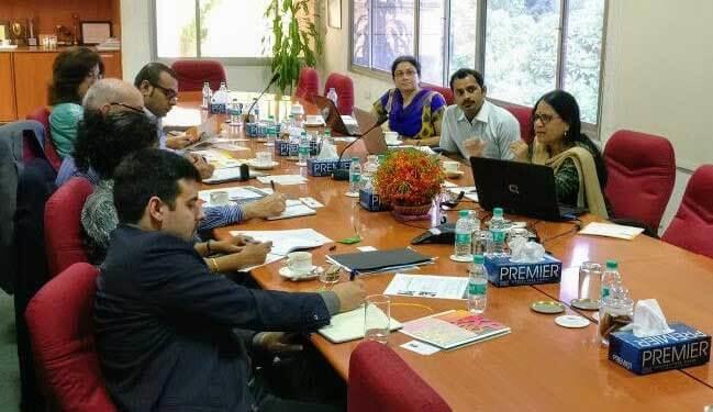 Business meeting at IKP Knowledge Park focused on India's biotech industry. Around a wooden conference table with red chairs, several professionals are engaged in discussion.