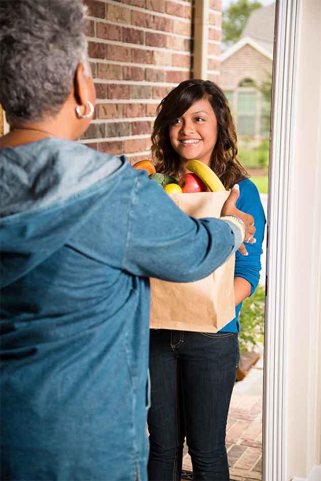 Smiling young woman delivers groceries to older woman at her home.
