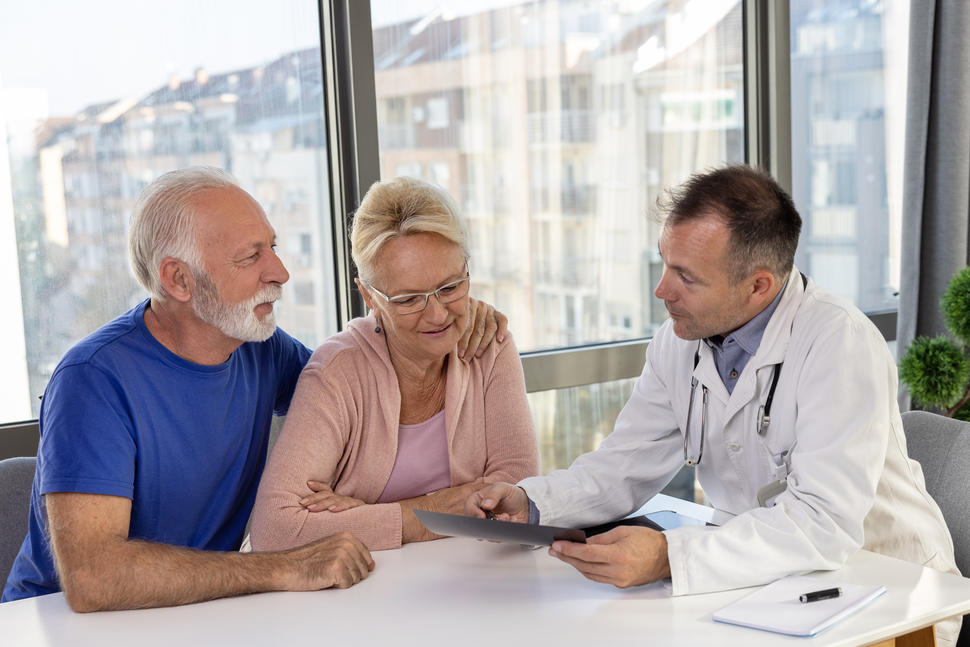 Older man and woman have a conversation with their doctor while seated at a table.